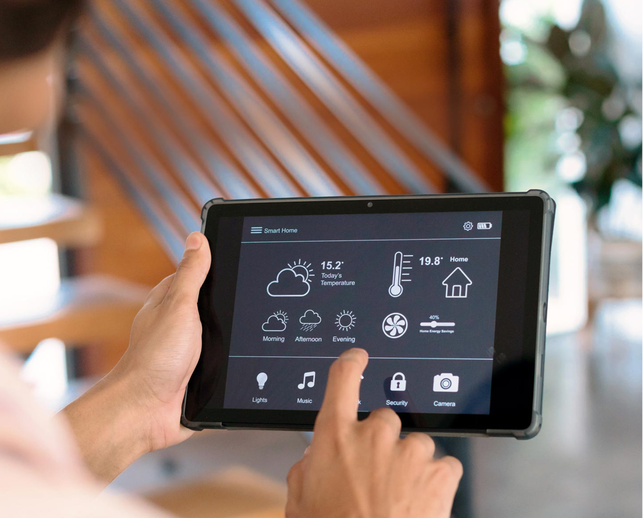 Eine Person bedient ein Tablet mit einer Smart-Home-App, die Wetter, Temperatur und verschiedene Steuerungsoptionen anzeigt. Beschreibung von KI generiert